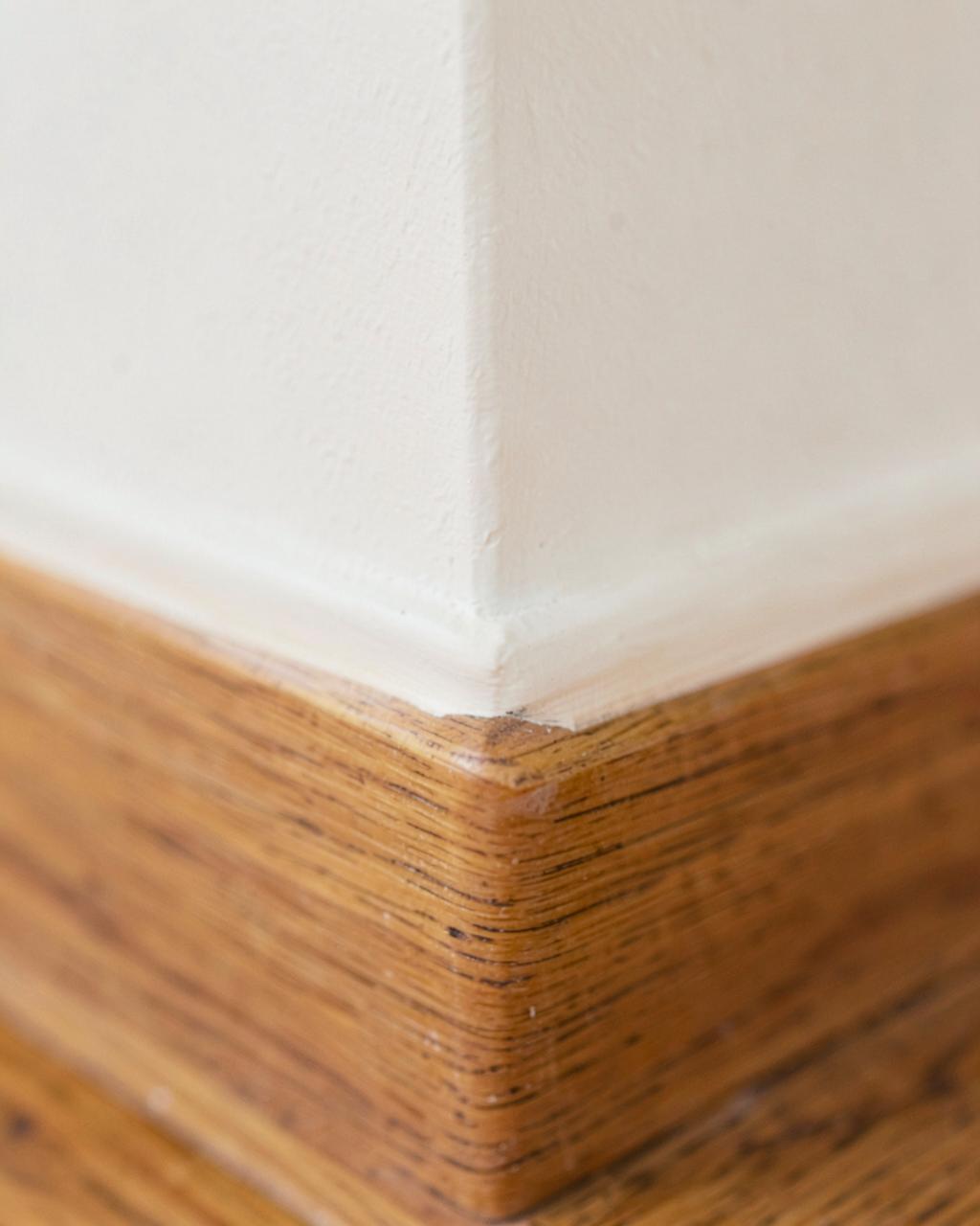 Crisp painted edge where an off-white wall meets a wooden skirting board